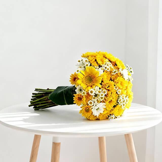Vibrant yellow and white daisy bouquet on a round white table in bright sunlight