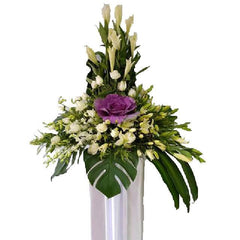 Elegant floral arrangement with purple brassica, white roses, lilies, and greenery in a tall vase