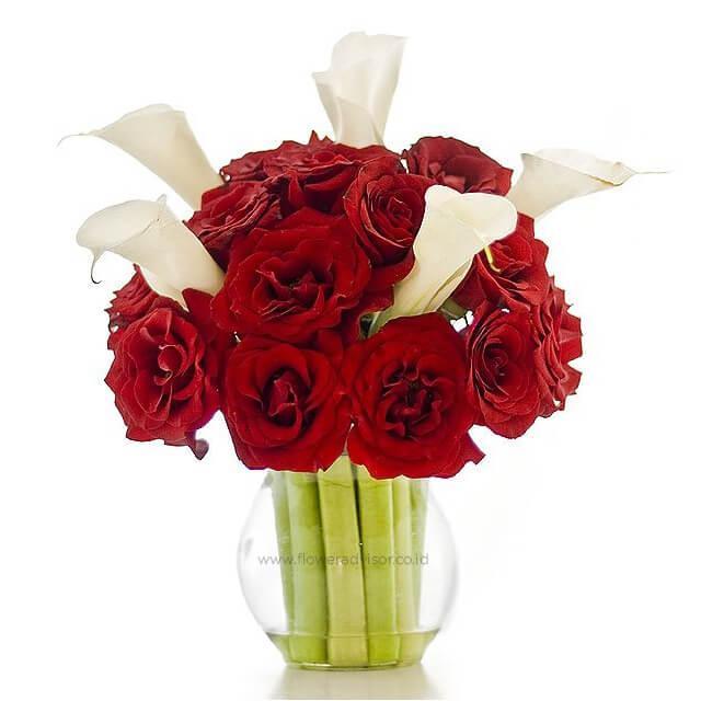 Bouquet of 18 red roses and 5 white lilies arranged in a clear glass vase