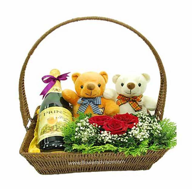 Gift basket with sparkling juice, two teddy bears, red roses, and greenery arrangement