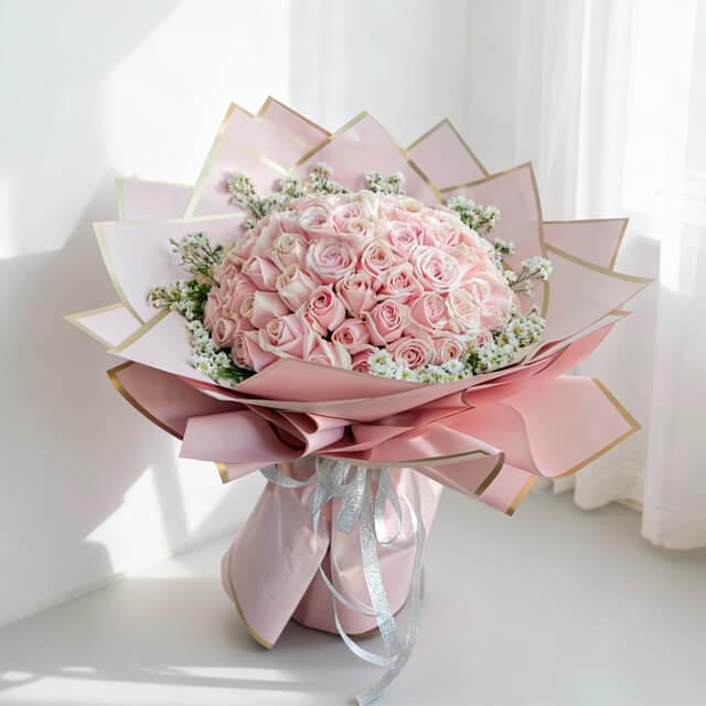 Elegant hand bouquet of 50 soft pink roses with white baby’s breath, wrapped in pink paper