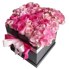 Pink roses and hydrangeas arranged in a black gift box with a pink and white ribbon