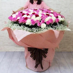 Large bouquet of pink and white roses with baby's breath in pink wrapping, held by a woman
