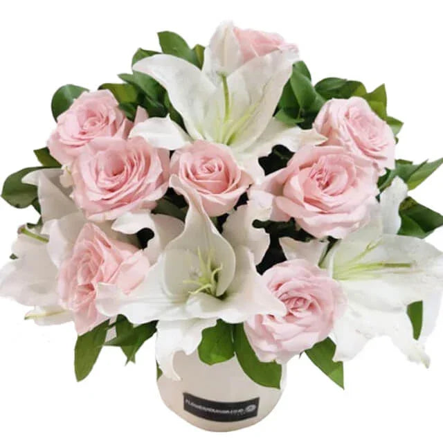 Bouquet of pale pink roses and white lilies in a round white flower box.