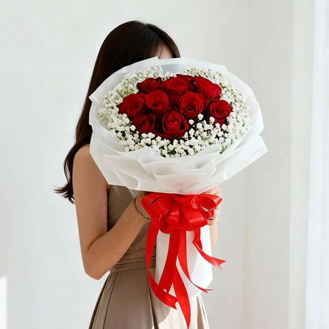 Woman holding a large bouquet of red roses and white baby's breath, wrapped in white paper with a red ribbon