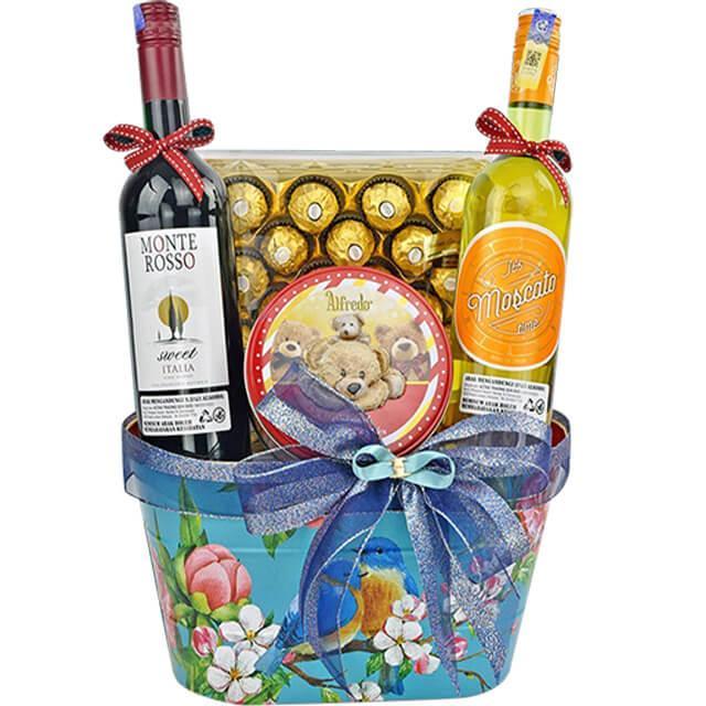 Gift basket with Monte Rosso red wine, Jo Moscato white wine, Ferrero Rocher chocolates, and teddy bear tin, decorated with blue floral basket and bows
