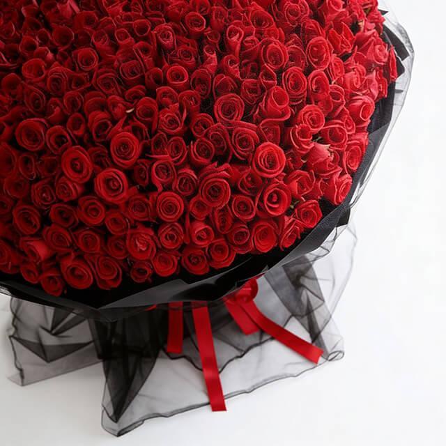 Large bouquet of red roses wrapped in black mesh with red ribbon, floral gift arrangement