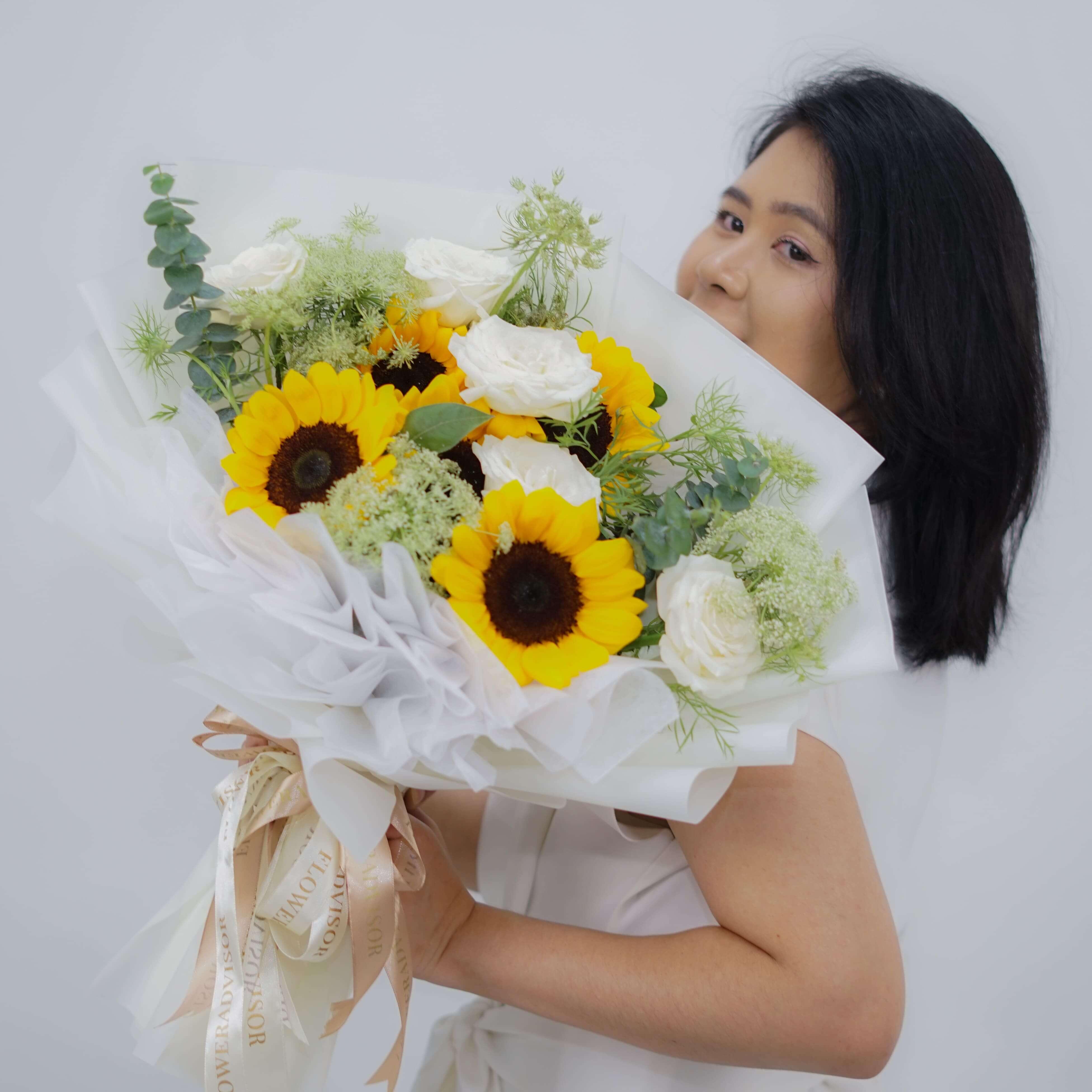 Woman holding a bouquet of sunflowers and white roses wrapped in white paper with decorative ribbons