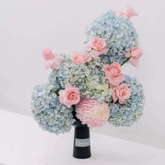 Elegant bouquet of blue hydrangeas and soft pink roses arranged in black vase on white background