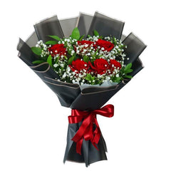 Hand-tied bouquet of red roses, baby's breath, and greenery wrapped in black paper with red ribbon
