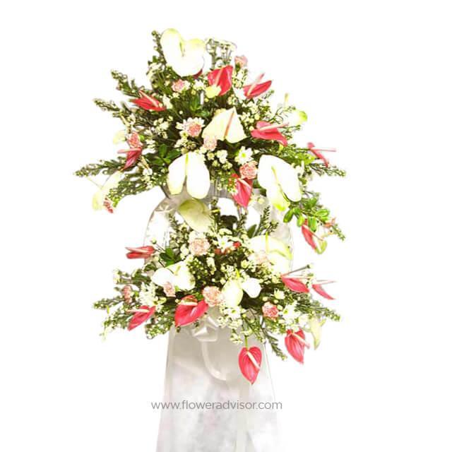 Elegant flower arrangement with white lilies, pink anthuriums, and greenery in a standing display