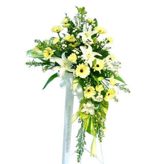 Elegant flower arrangement with white lilies, yellow daisies, greenery, and white ribbon