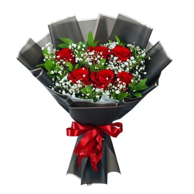 Bouquet of fresh red roses with baby's breath, green leaves, wrapped in black paper and a red ribbon