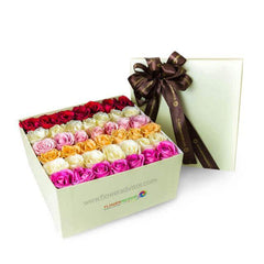 Square box of assorted fresh roses in pink, red, yellow, and white with a brown ribbon lid.