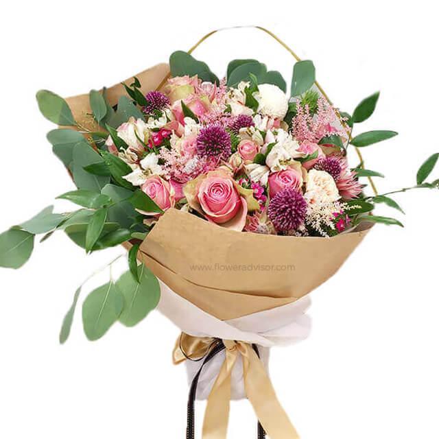 Mixed bouquet with pink roses, chrysanthemums, greenery, and wrapped in brown paper
